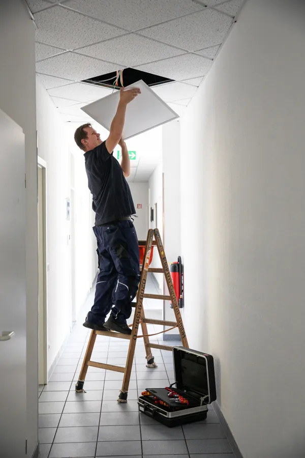Monteur auf der Leiter bei einer Beleuchtungssanierung im Flur